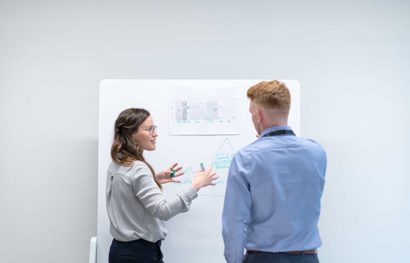 Two colleagues discussing a diagram on a whiteboard during a workshop